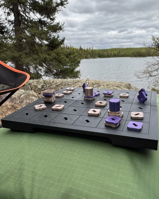 A black 3D-printed Tak travel set with purple and pink pieces on a lakeside rock